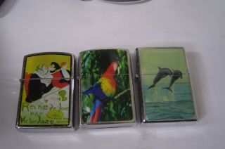 Three Fliptop Lighters With Designs Parrot / Dolphins And Toulouse - Lautrec